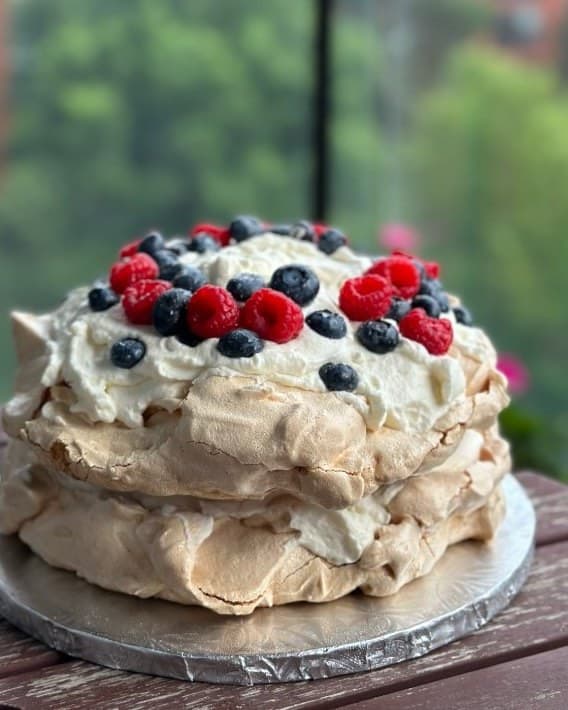 A pavlova topped with cream, raspberries, and blueberries